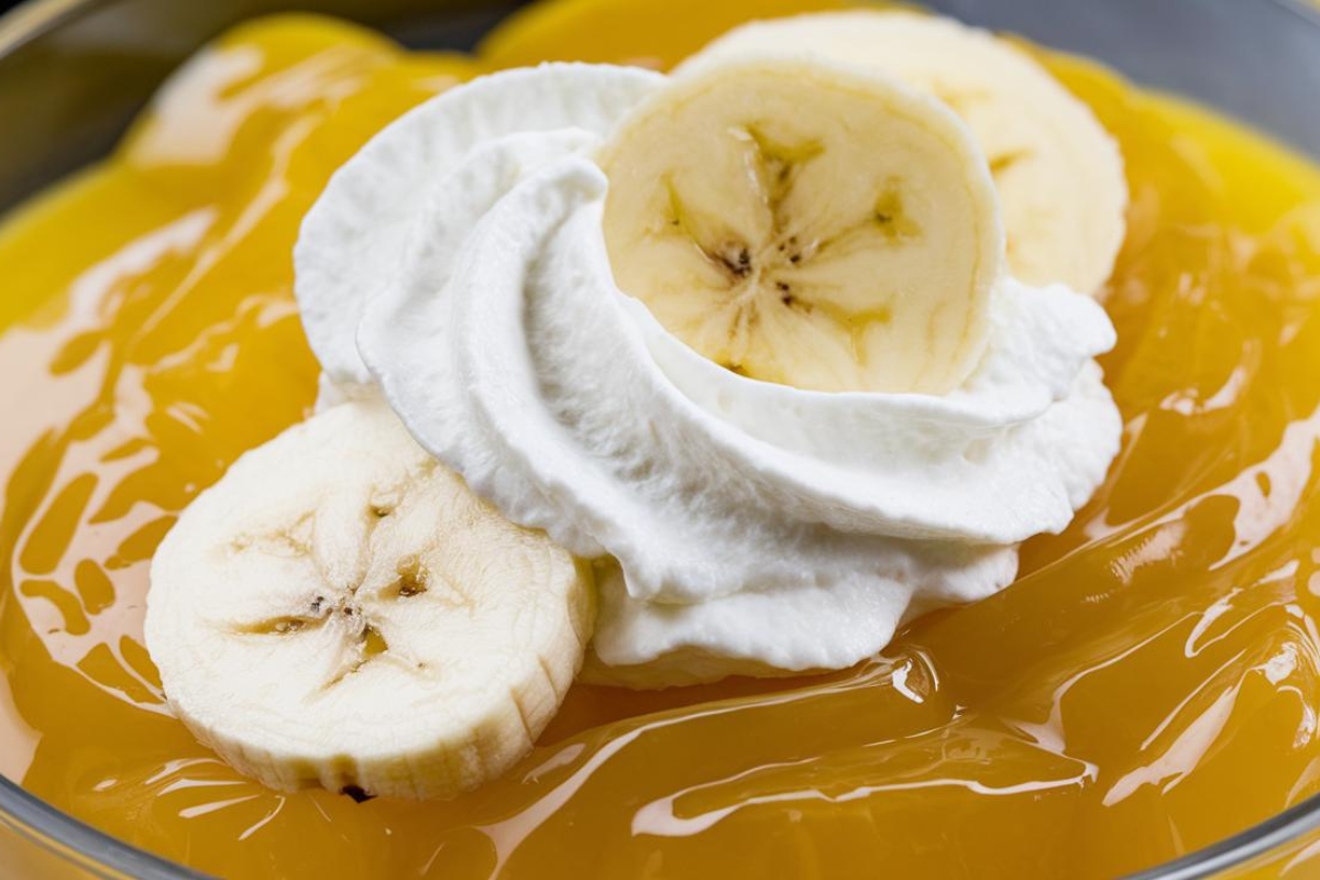 A close-up of a bowl of Banana Jell-O topped with whipped cream and banana slices.