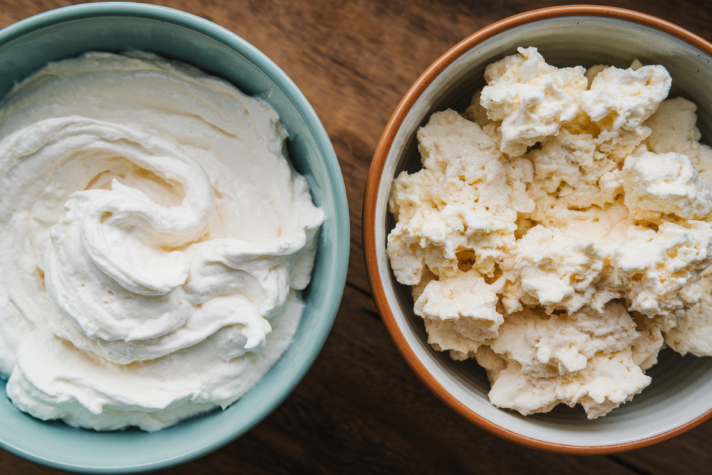 Smooth whipped cottage cheese next to regular chunky cottage cheese in two bowls, showing the difference in texture.

